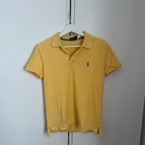 Gul pikétröja från Ralph Lauren - Säljer en snygg gul pikétröja från Ralph Lauren med klassisk krage och korta ärmar. Tröjan har en liten blå logga på bröstet och är perfekt för en avslappnad stil. Passar bra till både jeans och shorts. 🌟