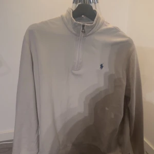 Beige tröja från Polo Ralph Lauren - Säljer en stilren beige tröja från Polo Ralph Lauren med halv dragkedja och broderad logotyp på bröstet. Perfekt för en avslappnad och snygg look.