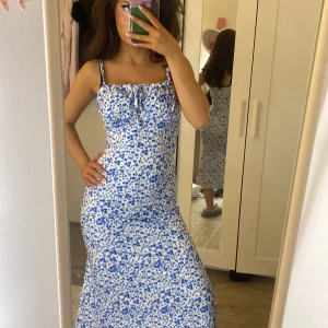 Blåvit blommig klänning - Säljer en vacker blåvit klänning med blommigt mönster. Klänningen har smala axelband och en knytning framtill. Perfekt för sommarens alla tillfällen! Pris kan diskuteras