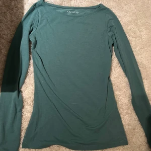 Grön långärmad topp från Orsay - Säljer en snygg grön långärmad topp från Orsay i deras Basic Style-kollektion. Perfekt för en enkel och bekväm look. Toppen har en rund halsringning och är tillverkad i ett mjukt material. 