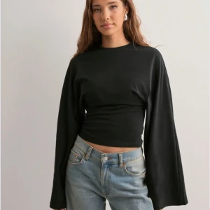 Svart långärmad topp - Snygg svart långärmad topp med en tight passform och vida ärmar. Perfekt för en stilren look. Passar bra till jeans eller kjol. Helt ny! Köpt för 299kr