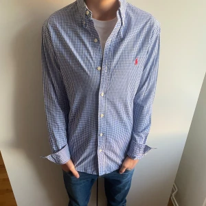 Ralph Lauren skjorta - Ralph Lauren skjorta i blått och vitt rutmönster med röd logga. Perfekt för både vardag och fest. Storleken är S slimfit och skjortan är i nyskick