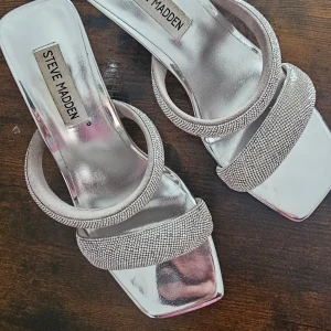 Silvriga klackskor från Steve Madden - Snygga silvriga klackskor från Steve Madden med glittriga remmar. Perfekta för att ge en touch av glamour till din outfit. De har en öppen tå och en elegant design som passar till många tillfällen.
