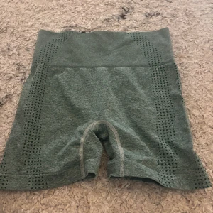 Gröna shorts med hög midja - Snygga gröna shorts med hög midja, perfekta för träning. Tillverkade i ett stretchigt material av polyamid och elastan. De har ett diskret mönster längs sidorna som ger en cool look.