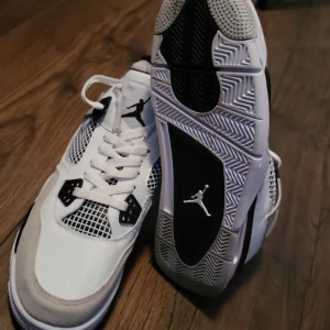 Nike Air Jordans i vit och svart - Snygga Nike Air Jordans i vit och svart med klassisk snörning och rund tå. Skorna har en stilren design med svarta detaljer och den ikoniska Jumpman-loggan på sulan.