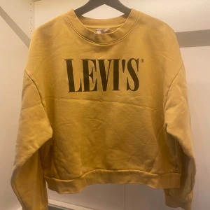 Gul sweatshirt från Levi's - Säljer en gul sweatshirt från Levi's med en stor logga på framsidan. Tröjan har en avslappnad passform och långa ärmar.