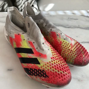 Färgglada fotbollsskor från Adidas - Säljer ett par iögonfallande fotbollsskor från Adidas med en mix av rött, gult och grått. Skorna har en strumpliknande passform och är dekorerade med svarta ränder på sidan. Perfekta för att dominera på planen med stil!