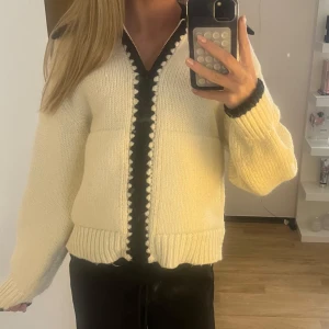 Stickad zip up cardigan - Säljer en mysig vit stickad kofta med svarta detaljer längs dragkedjan och kragen. Funkar både som en varm kofta eller en vårjacka då den värmer på ungefär samma nivå som en teddyjacka. Storlek 13-14 år men upplever som att den passar S. Använd fåtal gånger.