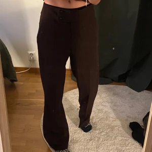 Bruna kostymbyxor med knappar - Snygga bruna kostymbyxor med diskret randigt mönster och knappar i midjan. Byxorna är en ullblandning och väldigt bekväma. 