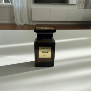 (1 kvar!!)Tom Ford Tobacco Vanille Eau de Parfum 100ml (pris kan snackas) - Säljer en elegant och lyxig parfymflaska från Tom Ford, Tobacco Vanille 100ml. Flaskan är mörkbrun med en fyrkantig form och har en gyllene etikett på framsidan. Korken är svart med en gyllene topp där märket är ingraverat. Perfekt för den som älskar varma och kryddiga dofter.