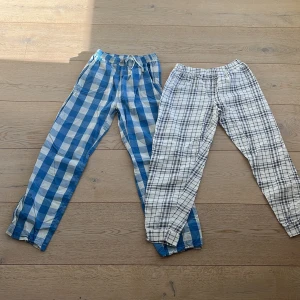 Två par rutiga byxor - Säljer två par rutiga byxor i olika färger. Ett par är blåvitrutiga och det andra är svartvitrutiga. Perfekta för en avslappnad stil. Byxorna har en bekväm passform och elastisk midja.