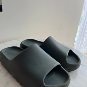 Yezzy slide - Säljer ett par stilrena svarta sandaler med öppen tå. Perfekta för en avslappnad look och bekväma att bära under varma dagar. Äkta skor box och kvitto finns! Priset är inte hugget i sten 