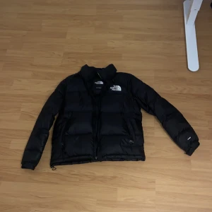 Svart dunjacka från The North Face - Säljer en svart dunjacka från The North Face. Jackan har en dragkedja framtill och är långärmad med en klassisk pufferdesign. Perfekt för kyliga dagar.
