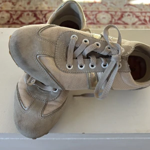 Beige sneakers från Geox - Snygga beige sneakers från Geox med snörning och detaljer i mocka och syntet. Skorna har en rund tå och en diskret logga på hälen. Perfekta för en stilren look.