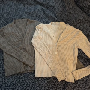 Ribbad kofta i beige och grå - Två ribbade koftor i beige och grå med knappar framtill. Perfekta för lager-på-lager under kyligare dagar. De har en v-ringad design och långa ärmar. 130kr för bägge!