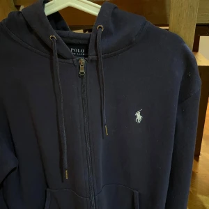 Mörkblå hoodie Polo Ralph Lauren - Säljer en snygg mörkblå hoodie från Polo Ralph Lauren. Den har dragkedja framtill och en klassisk logga broderad på bröstet. Meddela mig för meddelanden och frågor!