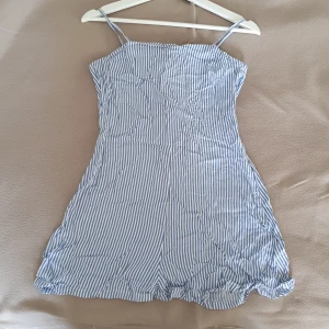 Blå- och vitrandig byxdress från H&M  - Säljer en söt blå- och vitrandig jumpsuit från H&M. Klänningen har smala axelband som kan justeras genom att knytas i ryggen.  Storlek 36. Använd 1 gång på skolavslutning 💙