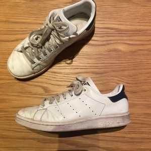 Vita Adidas Stan Smith sneakers - Säljer ett par klassiska vita Adidas Stan Smith sneakers med mörkblå detaljer på hälen. Skorna har snörning och en rund tå, vilket ger en tidlös look. Perfekta för en avslappnad stil. Använda därav priset❤️