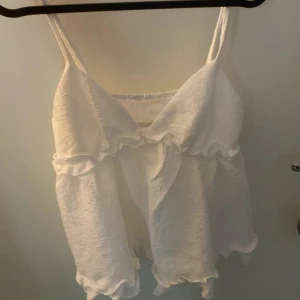 Vit ärmlös topp från Shein - Säljer en söt vit ärmlös topp från Shein. Toppen har volangdetaljer och smala axelband, perfekt för varma dagar. Materialet är mjukt och bekvämt, vilket gör den lätt att bära hela dagen.