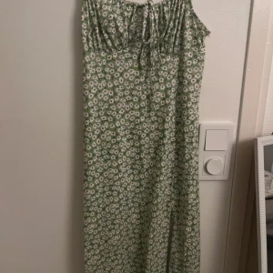 Grön klänning💚 - Super fin grön klänning med blommor på! Använd 1 gång! Fin slits i benet och detalj vid bröstet, går att knyta fram!💚 klänningen är mid lång!