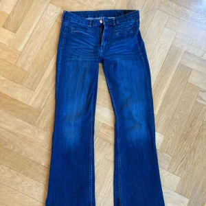 Blå bootcut jeans - Snygga blå bootcut jeans med klassisk femficksdesign och knappgylf. Perfekta för en avslappnad stil med en touch av retro. Passar bra till både sneakers och boots.