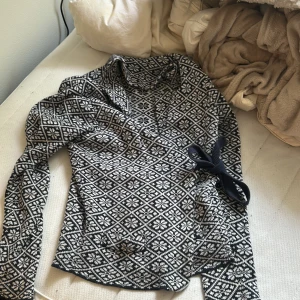 Mönstrad stickad kofta från STUTS - Säljer en svartvit stickad kofta från STUTS i storlek M. Koftan har ett snyggt geometriskt mönster, lång ärm och omlottmodell med knytband i sidan. Perfekt för dig som gillar klassiska nordiska vibes och vill ha något unikt i garderoben.