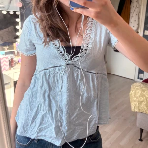 Ljusblå blus med spetsdetaljer - Supersöt ljusblå blus med v-ringning och fina spetsdetaljer längs halsringningen och ärmsluten. 