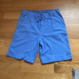 Blå shorts från Polo Ralph Lauren - Snygga blå shorts från Polo Ralph Lauren med bekväm resår och snörning i midjan. Tillverkade i mjuk bomull, perfekta för sommardagar. Klassisk design med sidofickor och en bakficka, samt den ikoniska loggan broderad framtill.