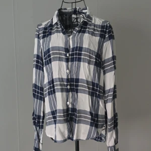 Blårutig skjorta med knappar - Snygg skjorta i blått och vitt med rutigt mönster och klassisk krage. Skjortan har långa ärmar och knäppning framtill. Perfekt för en avslappnad men ändå stilren look.