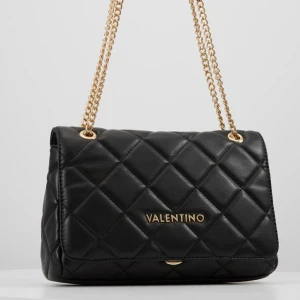 Svart Valentino Ocarina väska - Snygg svart axelväska från Valentino med quiltat mönster och guldfärgade kedjor. Väskan har ett elegant och stilrent utseende med logga framtill och dragkedja på insidan. Perfekt storlek för det viktigaste och ger en lyxig vibe till din outfit. Får plats med så mycket saker och går att använda vid speciella event liksom vardagligt💋💋(Har enbart använt ett par gånger och är i mycket bra skick, pris går självklart att diskutera)