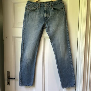 Levi's 502 ljusblå jeans straight fit - Ljusblå Levi's 502 jeans med klassisk femficksdesign och raka ben. Jeansen har en snygg tvättad look, bruna sömmar och läderpatch bak i midjan. Tillverkade i slitstark bomullsdenim och passar perfekt till en avslappnad stil.