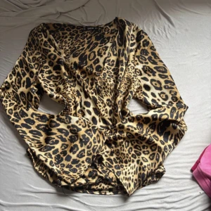 Leopardmönstrad omlottblus från SHEIN - Säljer en snygg leopardmönstrad omlottblus från SHEIN i beige och svarta toner. Blusen har lång ärm, v-ringning och ett flowy tyg som ger en cool look. Perfekt för dig som vill sticka ut med ett djurmönster och gillar trendiga detaljer.
