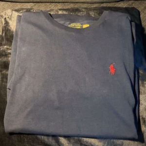 Mörkblå tröja Polo Ralph Lauren - Mörkblå långärmad tröja från Polo Ralph Lauren i bomull. Slim fit-modell med klassisk rund hals och rött broderat logotyp på bröstet. HELT oanvänd, köpt i helgen fysiskt på NK. Nypris 1000kr. Säljer pga för liten. Prislapp finns kvar men sitter ej kvar på tröjan pga det var tänkt som present. ☺️Ralph lauren papper medföljer. 