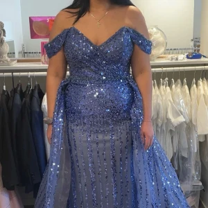 Blå glittrig balklänning offshoulder - Magisk blå långklänning med glittriga paljetter och offshoulder-modell. Klänningen har v-ringad urringning, markerad midja och voluminös kjol med släp. Perfekt för bal eller fest där du vill glänsa extra mycket. Köpt från diamar brud och fest. Endast buren 1 gång! 