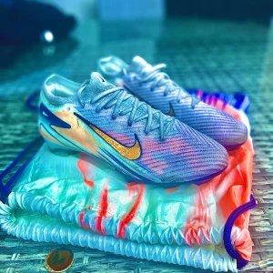 Nike Air Zoom Mercurial fotbollsskor - Snygga Nike Air Zoom Mercurial fotbollsskor i ljusblått och silver med guldigt Swoosh-märke på sidan. Skorna har snörning, mönstrad ovandel och platt sula med dobbar för grymt grepp på planen. Perfekta för dig som vill sticka ut med stil och prestanda.