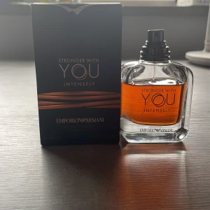 Emporio Armani Stronger With You - Emporio Armani Stronger With You Intensely är en elegant herrparfym i en stilren, transparent glasflaska med mörk bärnstensfärgad vätska. Flaskan har rundade former och svart spraykork. Medföljer gör en svart kartong med kopparfärgade detaljer. Finns cirka kvar 45/40 ml. Kan tänka mig frakta via betalning av swich eller annat. 
