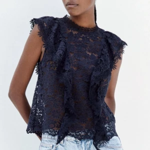 Mörkblå spetsblus från Zara XS - Supersnygg slutsåld mörkblå blus från Zara i spets med blommigt mönster och volangdetaljer framtill. Blusen är ärmlös med hög hals och knäppning bak i nacken. Perfekt att styla med jeans eller kjol för en trendig look. 🌸