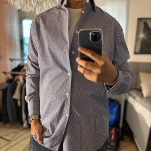 Blårutig skjorta från J.Lindeberg - Snygg blårutig skjorta från J.Lindeberg med klassisk krage och vita knappar. Skjortan är långärmad och har en stilren, tidlös look. Perfekt för dig som gillar en clean och dressad stil. Tillverkad i bomull för skön känsla hela dagen.