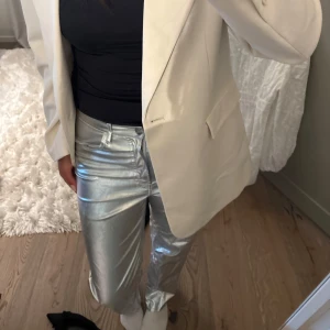 Silvriga byxor  - Säljer ett par riktigt snygga silvriga byxor i metallic-look. Byxorna har rak passform och normal midja, med klassisk knapp och dragkedja framtill. Sitter lågmidjade
