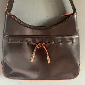 Svart skinnväska, Gabor - En jättefin handväska från Gabor i svart skinn med röda detaljer. Dragkedja och flera fack. Axelremmen är ca 67cm. Fåtal märken på framsidan som knappt syns, fler märken på baksidan som är lite tydligare.