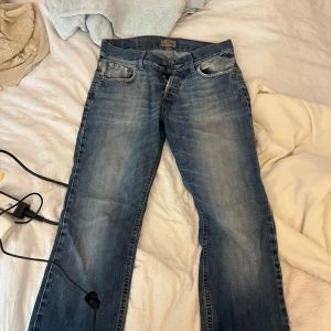 Blå jeans från Jack & Jones - Snygga blå jeans från Jack & Jones med klassisk femficksdesign och knäppning med knappar. Jeansen har en rak passform och slitna detaljer vid fickorna för en cool, avslappnad look. Perfekta till sneakers och hoodie.