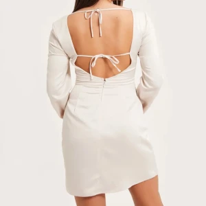 Satin klänning - Luscious satin dress i storlek 34/XS från Nelly. Krämfärgad/beige i färgen med snörning baktill. I mycket bra skick då den tyvärr aldrig kommit till användning. 