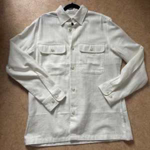 Vit overshirt från Jack & Jones - Stilren vit overshirt från Jack & Jones i linneblandning. Skjortan har klassisk krage, två bröstfickor med lock. Skit snygg till sommaren.använd 1 gång.Pris går att diskutera 