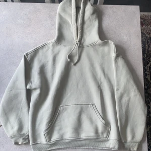 Ljusgrå hoodie med huva och ficka - En stilren ljusgrå hoodie med stor huva och dragsko, samt en klassisk känguruficka framtill. Tröjan har ribbade muddar vid ärmslut och nederkant. Mjuk insida i fleece för extra komfort. Perfekt för chill dagar eller när du vill ha en enkel och clean look.