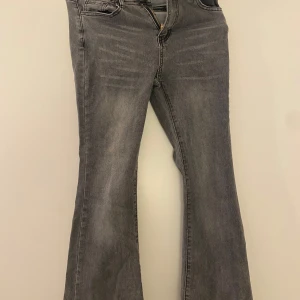 Grå bootcut jeans med utsvängda ben - Snygga grå jeans med bootcut-modell och utsvängda ben. Jeansen har klassisk femficksdesign, dragkedja och knapp framtill samt diskreta slitningar för en cool look. Perfekta för dig som gillar en retrostil med modern twist.