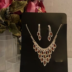 Glittrigt halsband och örhängen set - Snyggt smyckeset med halsband och matchande örhängen i guldton med glittrande stenar och bruna, droppformade kristaller. Perfekt för att sticka ut med extra bling och passar till fester, bröllop, bal…