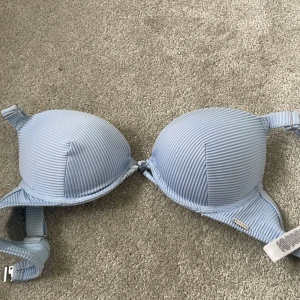 Ljusblå randig bikini överdel från NewYorker - Säljer en ljusblå bikini överdel från NewYorker med tunna vertikala ränder och vadderade kupor. Bikini överdelen har justerbara axelband och klassisk knäppning bak. Materialet är mjukt för extra komfort. Perfekt för dig som gillar en enkel men snygg look.