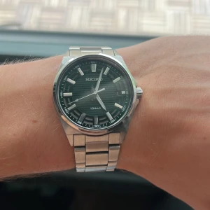 Seiko klocka med grön urtavla - Stilren Seiko klocka med grön urtavla och tydliga index. Boetten och länken är i silverfärgat rostfritt stål. Klockan har en sportig känsla med robust länk och klassisk design. Perfekt för dig som gillar snygga accessoarer med lite edge.