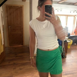 Grön omlottkjol från NA-KD - Snygg grön kort omlottkjol från NA-KD i lätt och skönt material. Kjolen har knyt i sidan och en enkel, stilren look som passar perfekt till varma dagar. Perfekt att matcha med en crop top eller t-shirt för en fräsch sommarstil.