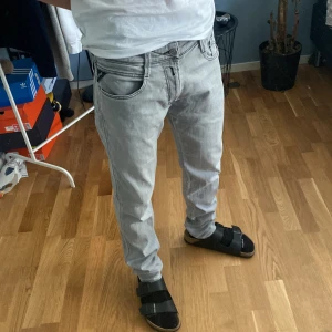 Replay Anbass ljusgrå slim jeans - Säljer ett par Replay Anbass jeans i ljusgrå tvätt. Modellen är slim fit med klassiska fem fickor och snygga detaljer på bakfickorna. Jeansen har normal midja och är tillverkade i mjukt denimtyg som sitter skönt hela dagen.